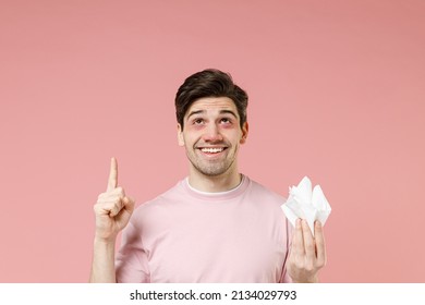 Smiling Happy Sick Ill Allergic Man Has Red Eyes Runny Nose Suffer From Allergy Hold Paper Napkin Pointing Finger Above On Workspace Promo Advert Area Isolated On Pastel Pink Color Background Studio