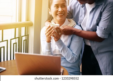 Smiling And Happy South East Asian Senior And Elderly Husband And Wife Couple Holding Each Other While One Is Using Laptop - Senior Elders Togetherness Concept