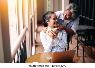 Smiling And Happy South East Asian Senior And Elderly Husband And Wife Couple Holding Each Other While One Is Using Laptop - Senior Elders Togetherness Concept