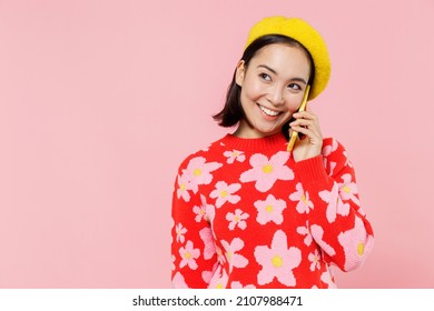 Smiling Happy Woman Of Asian Ethnicity 20s Wear Red Knitted Sweater Beret Talk Speak On Mobile Cell Phone Conducting Pleasant Conversation Isolated On Plain Pastel Pink Background Studio Portrait.