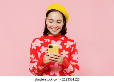 Smiling happy woman of Asian ethnicity 20s wear red knitted sweater beret hold in hand use mobile cell phone isolated on plain pastel pink background studio portrait. People lifestyle fashion concept - Powered by Shutterstock