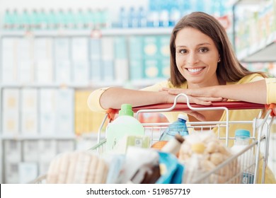 Smiling Happy Woman Enjoying Shopping At The Supermarket, She Is Leaning On A Full Cart, Lifestyle And Retail Concept