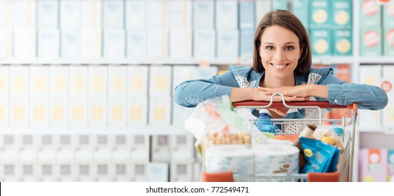 Smiling Happy Woman Enjoying Shopping At The Supermarket, She Is Leaning On A Full Cart, Lifestyle And Retail Concept