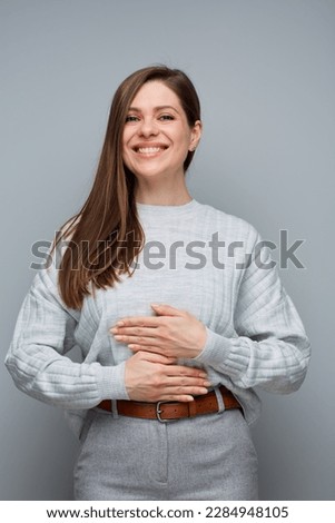 Smiling happy woman holding hands on stomach. isolated portrait on gray.