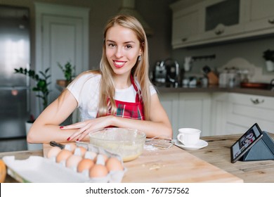 Smiling happy woman with long hair and red lips posing at camera on the background of the kitchen, in the foreground ingredients of dish, real emotions - Shutterstock ID 767757562