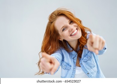 Smiling happy woman pointing at the camera with both hands and her head tilted to the side with a playful expression and focus to her face over grey