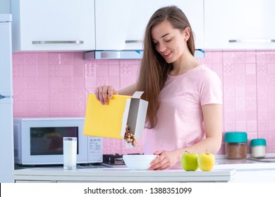 Smiling, happy woman pouring frosted chocolate balls out of the cereals box for healthy cereals breakfast in morning at home - Powered by Shutterstock