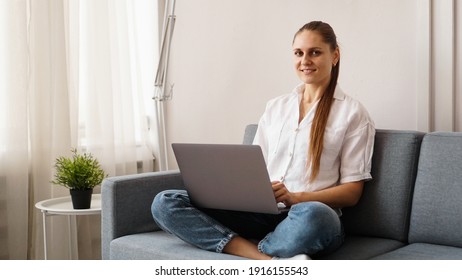Smiling happy woman sitting on the sofa and using laptop. The concept of remote work or study during quarantine.