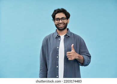 Smiling happy young adult arab man professional employee or student standing isolated on blue background showing thumbs up like hand gesture giving recommendation advertising good service or result. - Powered by Shutterstock