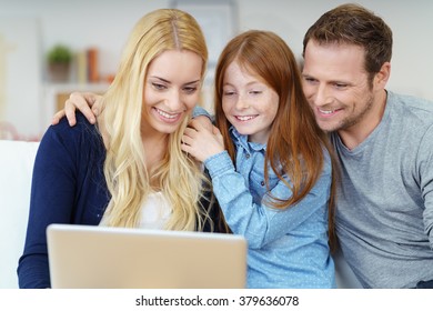 Smiling Happy Young Family Enjoying Surfing The Internet On A Laptop Computer As They Relax Together At Home On A Sofa