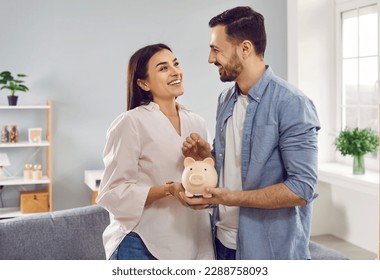 Una joven familia joven sonriente y feliz juntó monedas en un banco de cerdos para ahorrar dinero. Las parejas casadas están planeando ahorrar dinero. Ahorro, inversiones, libertad financiera, negocios, esperanza de éxito.