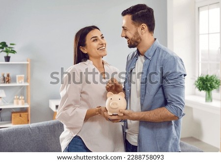 Smiling, happy young family together put coins in piggy bank to save money. Married couple are planning to save up finances. Savings, investments, financial freedom, business, hope for success.