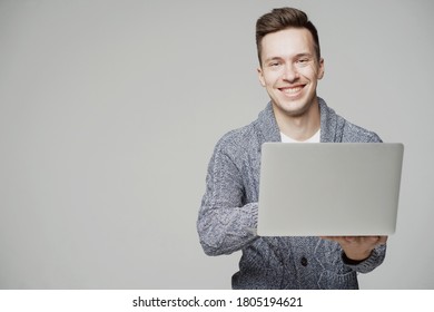 Smiling Happy Happy Young Guy Of European Appearance, Working On A Laptop. Grey Jacket, Good Mood. Solid Color Background