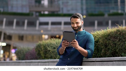 Smiling happy young indian business man professional, eastern latin businessman executive standing outdoors in city park holding using digital tablet online technology in night city park. - Shutterstock ID 2197444709