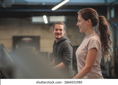 Smiling And Happy Young Mixed Ethnicity Couple Jogging On Treadmills In Modern Indoor Gym And Talking With Each-other. Healthy And Active Lifestyle