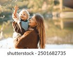 Smiling happy young mother 24-26 year old holding baby girl over lake and nature background. Autumn season. Motherhood. 