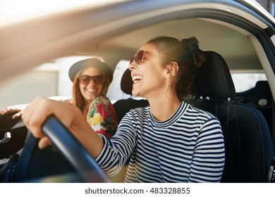 Smiling happy young woman giving her friend a lift in her car in town, profile view through the open side window with sun flare - Shutterstock ID 483328855