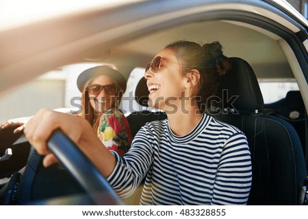 Smiling happy young woman giving her friend a lift in her car in town, profile view through the open side window with sun flare