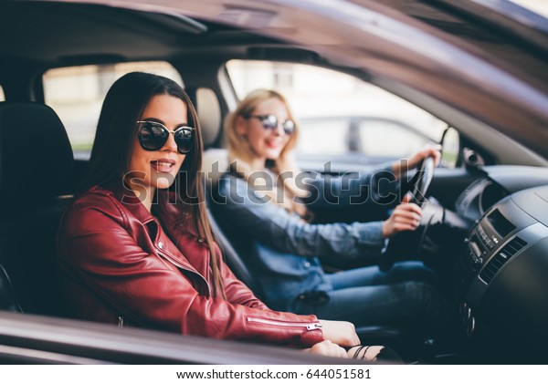 Smiling happy young woman giving her friend a lift\
in her car in town, profile view through the open side window with\
sun flare