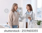 Smiling healthcare worker with tablet supporting senior patient in hospital