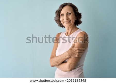 Smiling healthy mature older senior happy woman showing bandage on arm after getting vaccination. Vaccine and old elder people inoculation, elderly immunity for covid prevention concept. Portrait