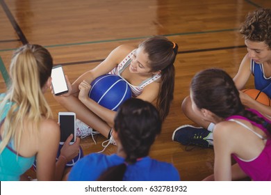 Smiling high school girls looking at the mobile phone while relaxing in the basketball court - Powered by Shutterstock