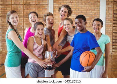 Smiling high school kids holding trophy in basketball court
