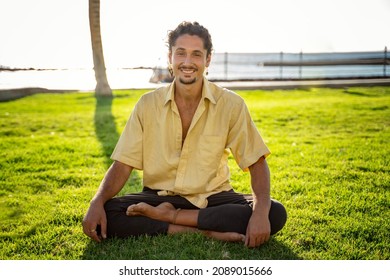 Smiling Hippie Italian Man Sitting In Lotus, Practicing Yoga Outdoor On Sunny Day. Men Looking At The Camera With Cute Smile. A Lot Of Copy Space.