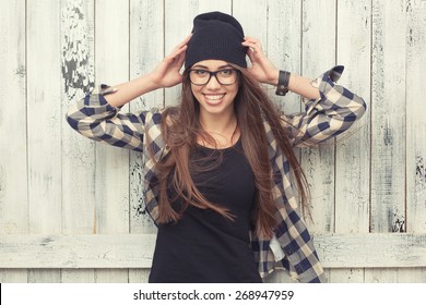 Smiling hipster girl in glasses and black beanie on the wooden background