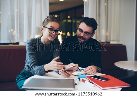 Smiling hipster girl holding mobile phone in hand feeling good from received funny message, woman using  smartphone connected to 4g internet at university cafeteria spending time with boyfriend