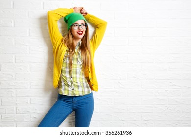 Smiling Hipster Girl at White Brick Wall Background. Street Syle. Trendy Casual Fashion Outfit in Spring or Autumn. Copy Space.