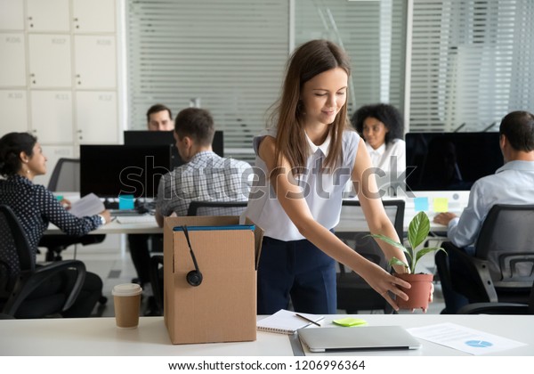 Smiling hired female company employee unpacking\
box with personal belongings at workplace on first working day in\
shared office, happy intern or newcomer got new job excited to\
start work concept