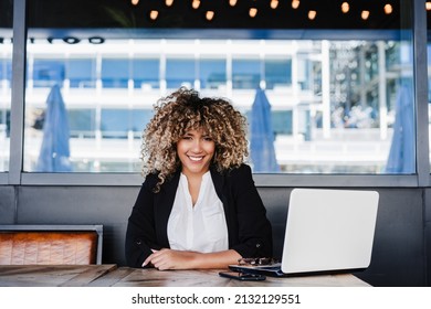 Smiling Hispanic Business Woman In Cafe Working On Laptop And Mobile Phone. Tech And Lifestyle