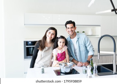 Smiling Hispanic Family With Daughter Cooking Food In Kitchen At Home