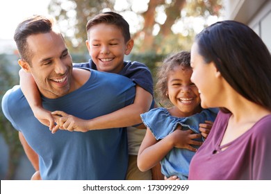 Smiling Hispanic Family With Parents Giving Children Piggyback Rides In Garden At Home - Powered by Shutterstock