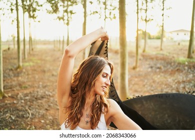 Smiling Hispanic Female With Long Wavy Hair Raising Arm While Dancing With Veil Against Tree In Evening