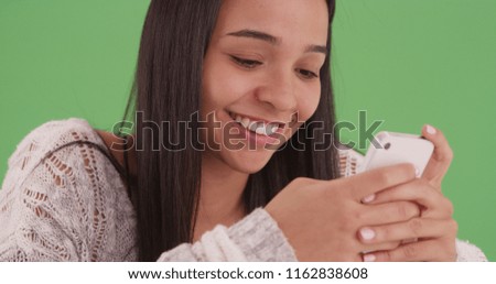 Smiling hispanic girl smiles while she looks on her smart phone on green screen
