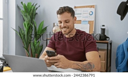 Smiling hispanic man with beard using smartphone in modern office setting