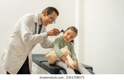 Smiling hispanic pediatrician examining kid ear with otoscope, child at doctor's office. Latin doctor checking girl ear using an auroscoper. - Powered by Shutterstock