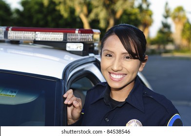 улыбающийся латиноамериканский полицейский рядом с патрульной машиной.