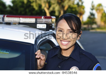 a smiling Hispanic police officer next to her patrol car.