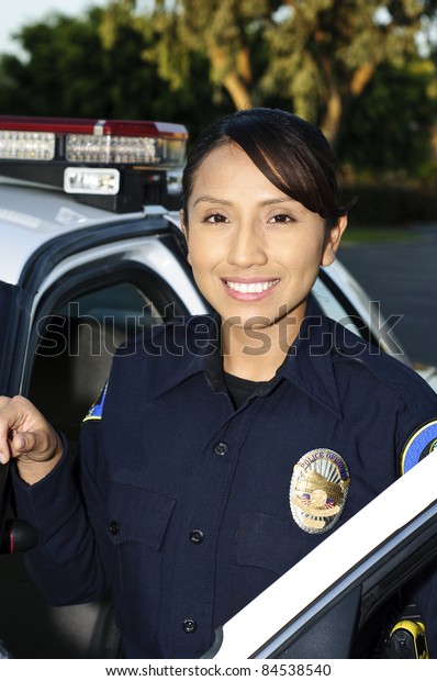 a\
smiling Hispanic police officer next to her patrol\
car.