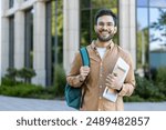 Smiling hispanic student stands outside academic building holding backpack and notebooks. Concept of higher education, confidence, and youth. Ideal for educational and lifestyle themes.