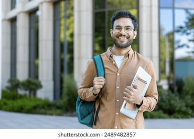 Smiling hispanic student stands outside academic building holding backpack and notebooks. Concept of higher education, confidence, and youth. Ideal for educational and lifestyle themes.