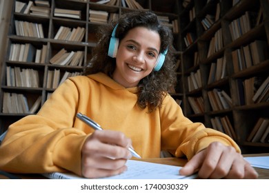 Smiling Hispanic Teen Girl School Student Wear Headphones Looking At Webcam Distance Learning. Zoom Video Call Remote Class, Online Lessons And Courses Concept. Headshot Portrait. Webcamera View.