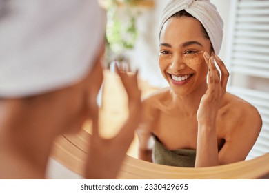 Smiling hispanic woman applying under eye collagen mask and looking at mirror. Attractive young mexican woman taking care of her skin by applying anti-fatigue under eye patch. - Powered by Shutterstock