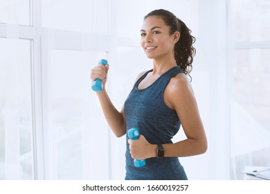 Smiling Hispanic Woman With Dumbbells On Her Workout Indoors, Space For Text