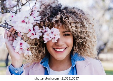 Smiling Hispanic Woman With Eyes Closed In Park Enjoying Sunny Day. Spring Flowers Background