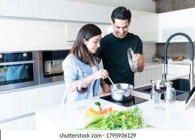 Smiling Hispanic Young Couple Cooking Food At Home