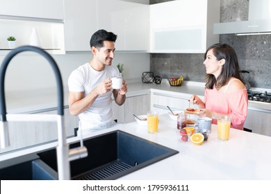 Smiling Hispanic Young Couple Having Breakfast At Kitchen Island